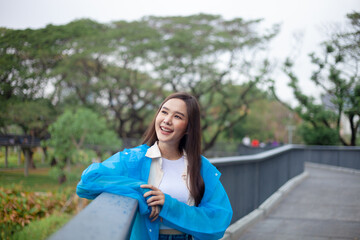 A woman in a blue raincoat is smiling and looking out over a bridge. Scene is cheerful and uplifting