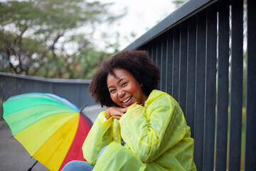 A woman is sitting on a railing with a rainbow umbrella next to her. She is smiling and she is enjoying the moment