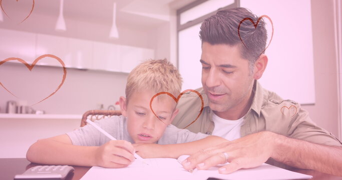 Image of hearts falling over caucasian man and his son doing homework - Powered by Adobe