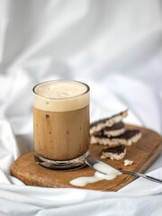 Close-up shot of a cold brewed coffee latte in a glass on a wooden board on the white bedsheets