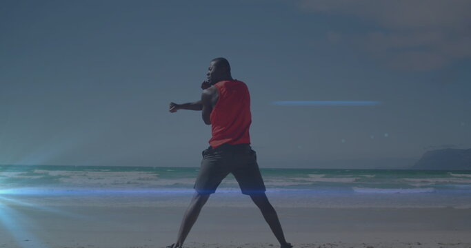 Image of blue light spot against rear view of african american fit man stretching at the beach