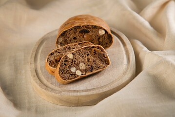 Brown wooden plate with freshly-cut slices of bread on top, resting on a beige cloth
