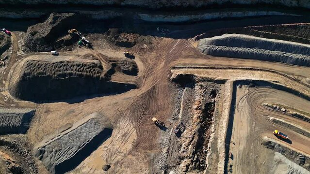 Drone footage over an Excavator working on an open pit mine, quarry stone mining on dirt ground