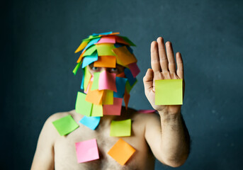 Man with colorful sticky notes all over his face and body show palm hand making stop gesture - 767959925