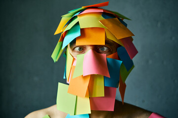 Close up portrait of man with cross-eyed covered with colorful sticky notes all over his face and head - 767959933
