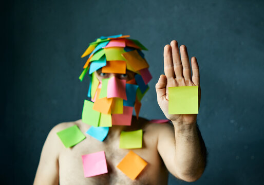 Man with colorful sticky notes all over his face and body show palm hand making stop gesture