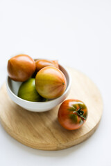 Fresh daejeo tomato in a white bowl under warm sunlight indoor natural light on white background