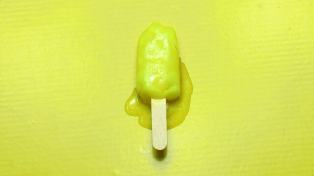 Isolated time lapse video of a lemon lime ice cream slowly dewatering, seen from above, on yellow background