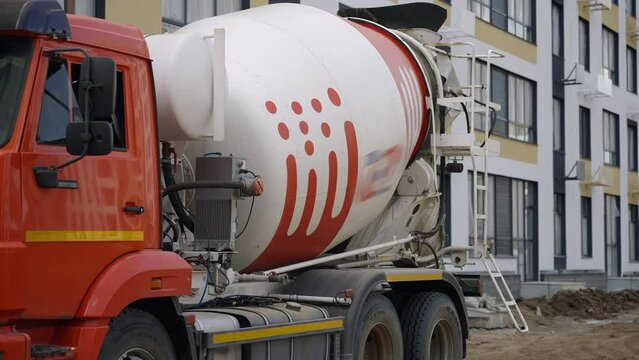 A red and white wheel fixture motor vehicle, a concrete mixer truck, is parked in front of a building. The vehicles tires have a sturdy tread for navigating asphalt roads