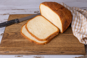 Wheat (white) bread with a crispy crust on a wooden board, cut into slices. Homemade baking in rustic style. Selective focus, close-up.