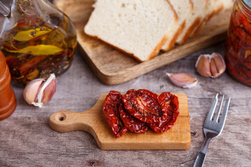 Sun-dried tomatoes in olive oil on a mini board with homemade bread in a rustic style. Traditional home cooking. Selective focus, close-up.