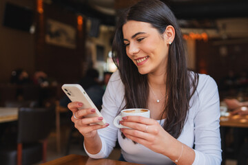 A one young girl or woman is drinking coffee in cafe or restaurant while using her phone to send messages