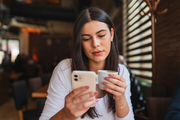 A one young girl or woman is drinking coffee in cafe or restaurant while using her phone to send messages
