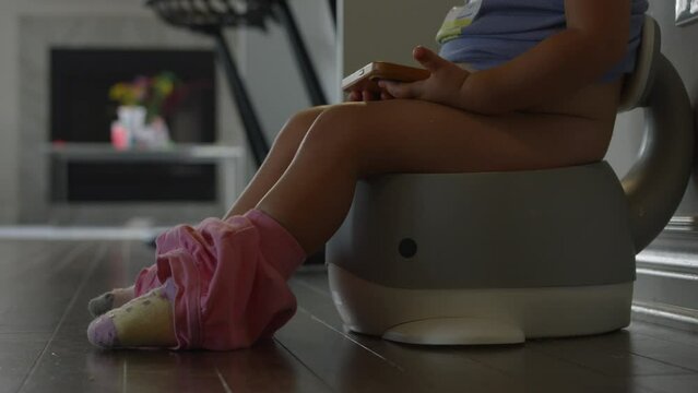 Toddler girl sits on potty watching smart phone - potty training - side profile