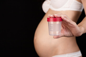 Pregnant, nude woman holding a test jar with a red cap on a dark wall background. Medical concept.