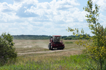 Red harvester on a rural field, harvesting grain on a sunny summer day, driving along the road.