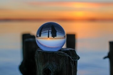 Crystal clear lensball atop a wooden post with sunset above the sea in background
