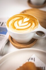 Closeup of a white mug of latte coffee on a wooden surface under the bright light