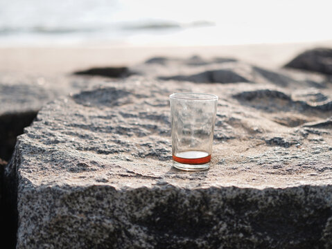 Almost empty glass of black tea on a rock by the beach