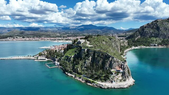 Aerial drone cinematic video of iconic Acronafplia fortress overlooking old city of Nafplio below famous castle of Palamidi as seen at morning with beautiful clouds and deep blue sky, Argolida, Greece