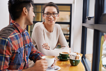 Happy couple, window and relax with coffee at cafe for chatting, talking or social bonding. Young...