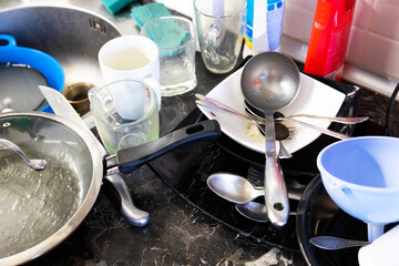 A pile of dirty dishes in the metal sink and on the table is pouring. Kitchen after breakfast, lunch, dinner. Clean dishes concept.