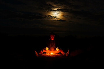 A man sits on against a burning candle on a dark night. Mystic concept.