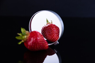 Red strawberries on a black background with reflection in the mirror. The concept of beauty and perfection. Selective focus