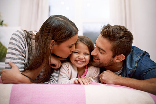 Kiss, parents or kid in bed to smile, lying or relax as happy, hug or bonding together in house. Young family, cheek or care to embrace, playful or parenting in childhood on joyful, break or getaway