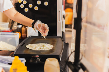 Chef sprinkles a tortilla with cheese preparing fresh quesadilla on black grill.