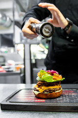 Professional chef finalizing a gourmet burger in a kitchen, demonstrating culinary expertise and...