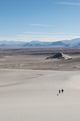Fototapeta na wymiar Personas caminando a lo lejos en un desierto. Montañas de fondo. 
