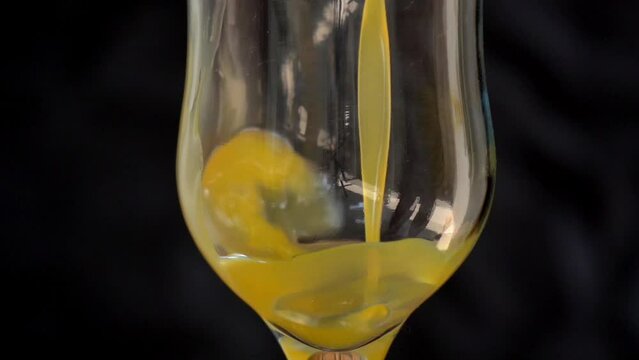 Fresh mango juice pours into a glass against a black background. Pouring orange juice stream from jug into glass with blurred black background. slow motion