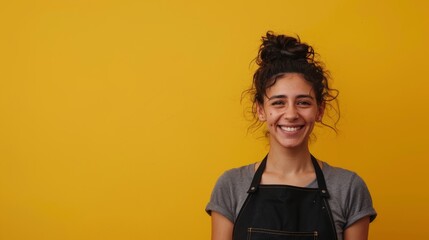Portrait of a girl with an apron for a waiter laughing while posing on a yellow background, 
