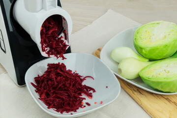 Beets, onion and cabbage in a vegetable cutter on kitchen table. Chopped beet is falling into a...