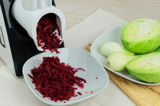 Beets, onion and cabbage in a vegetable cutter on kitchen table. Chopped beet is falling into a bowl. Homemade healthy food. Healthline.