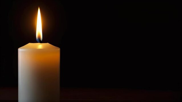 Closeup single white candle burning. Isolated candle burning on a black background, copy space. White paraffin candle with yellow shades burns on dark background. slow motion. Remembrance Day