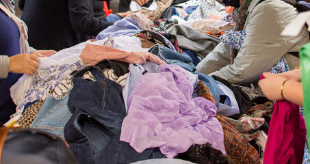 Back view of people looking at a pile of second hand clothes in a flea market.