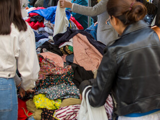 Back view of unrecognocible people looking at a pile of second hand clothes in a flea market.