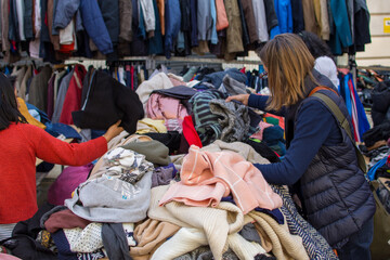 Back view of people looking at a pile of second hand clothes in a flea market.