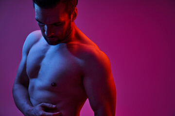 portrait of seductive man with bristle and bare chest posing on purple backdrop with lights