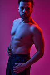 portrait of shirtless man posing in pinstripe trousers on purple backdrop with red and blue lights