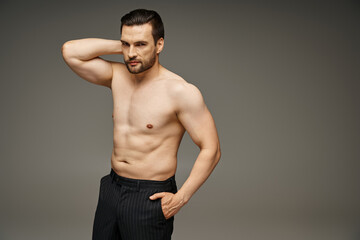 portrait of brunette handsome man with bare chest posing with hand in pocket on grey background
