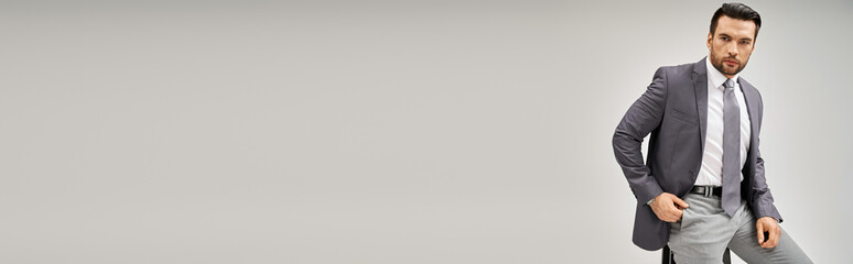 handsome and confident businessman in formal wear leaning on high stool on grey background, banner