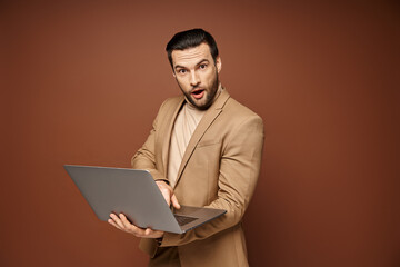 shocked and handsome professional using his laptop while working remotely on beige background