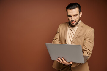 focused and handsome professional using his laptop while working remotely on beige background