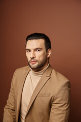 portrait of attractive man in elegant attire looking at camera on beige backdrop, handsome executive