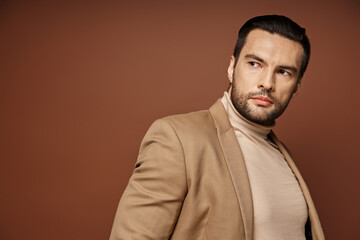 Fototapeta premium handsome man in elegant attire looking away while posing in blazer on beige background