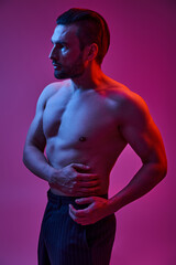 seductive man with bare chest posing in pinstripe trousers on purple backdrop with red lights