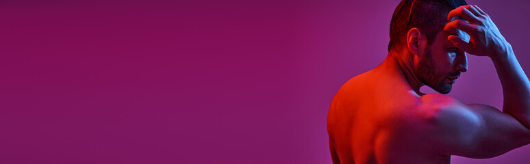portrait of muscular and shirtless man posing on purple background with red and blue lights, banner